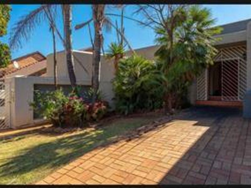 Front exterior view of the property featuring a paved driveway, established garden, and secure gated entrance.