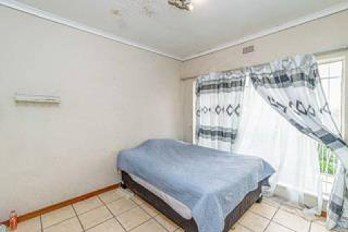 A bedroom featuring tiled flooring and a sliding glass door with security gate, showing signs of ceiling water damage and worn wall finishes.