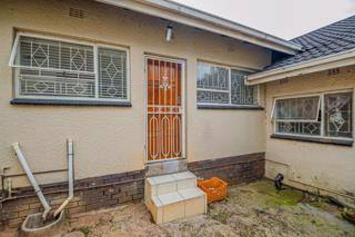 Rear exterior view of the property featuring security gates, tiled entrance steps, and brick foundation detailing.