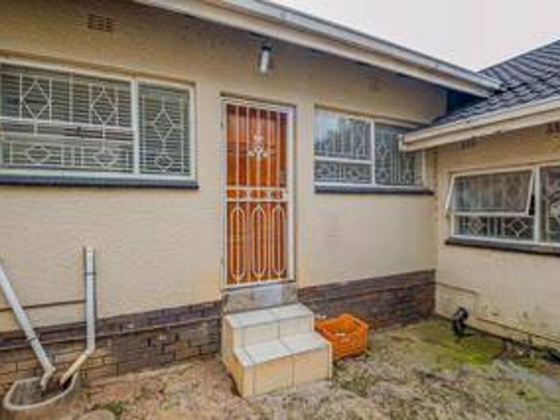 Rear exterior view of the property featuring security gates, tiled entrance steps, and brick foundation detailing.