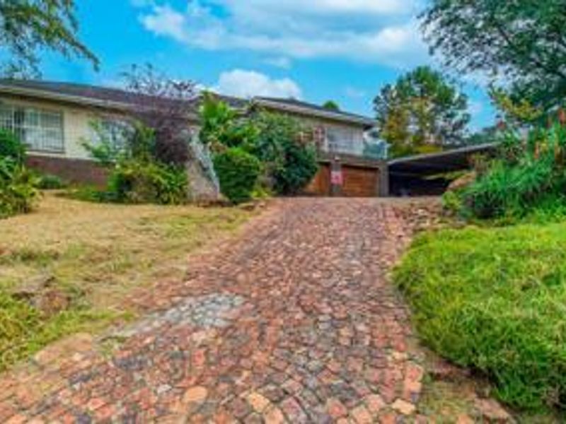 Front view of a residential property featuring a cobblestone driveway, double garage, attached carport, and established garden landscaping.