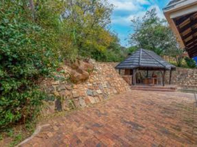 A spacious rear patio featuring brick paving, a stone retaining wall, and a covered gazebo with a built-in braai area.