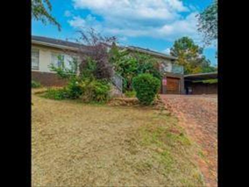 Front exterior view of the house featuring a brick driveway, garage, and covered carport area with established garden landscaping.
