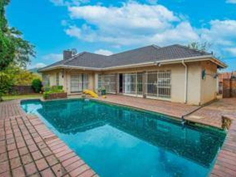 Rear exterior view featuring a swimming pool, brick paved surround, and a single-story house with a tiled roof and security gates.