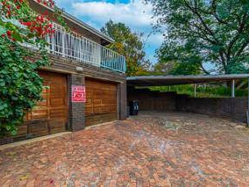 Exterior view of a double garage with an attached carport and brick paved driveway, featuring a balcony above the garage area.