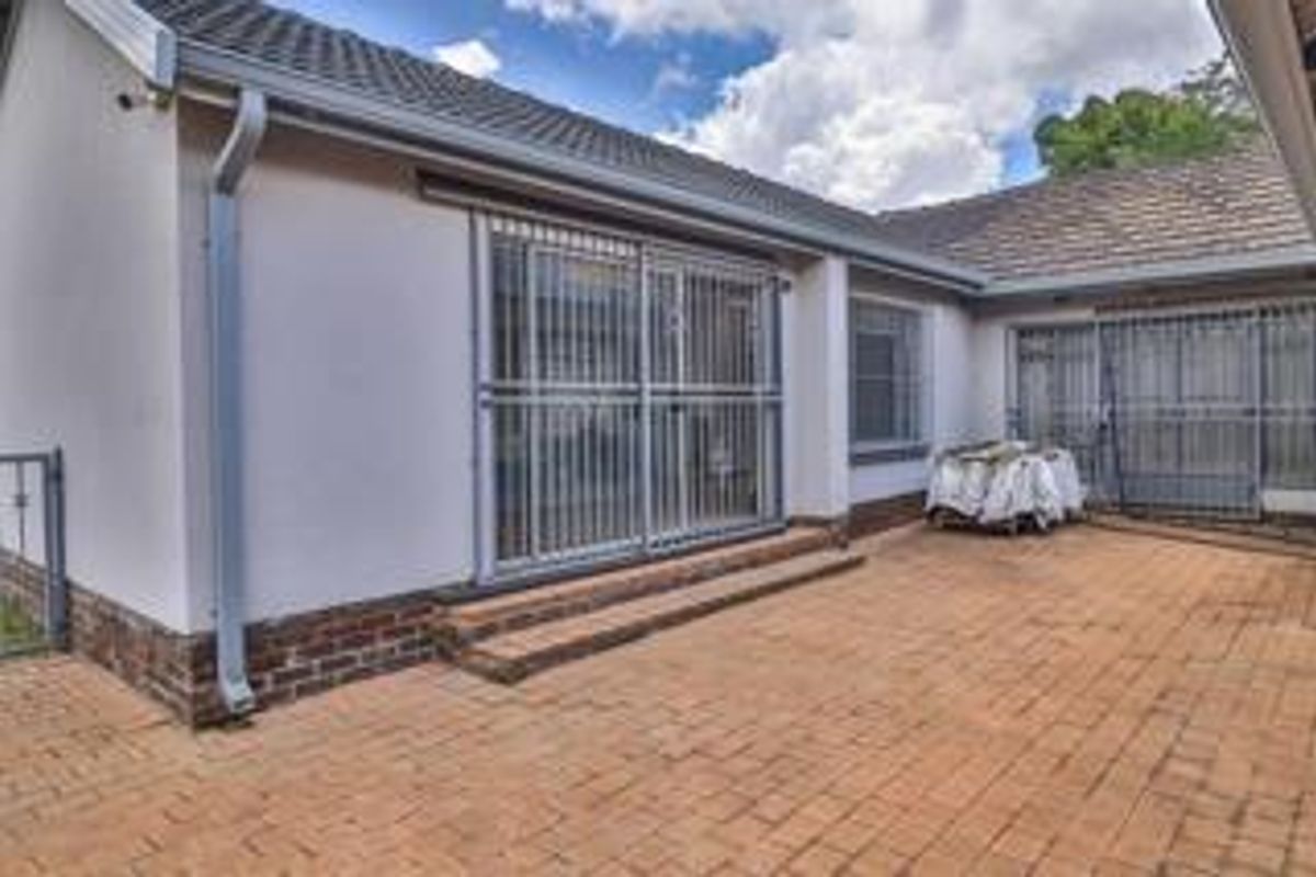 A rear exterior view of the property featuring brick paving, sliding glass doors with security gates, and a tiled roof.