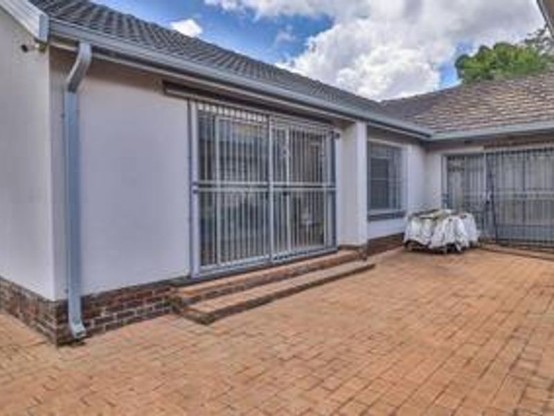 A rear exterior view of the property featuring brick paving, sliding glass doors with security gates, and a tiled roof.