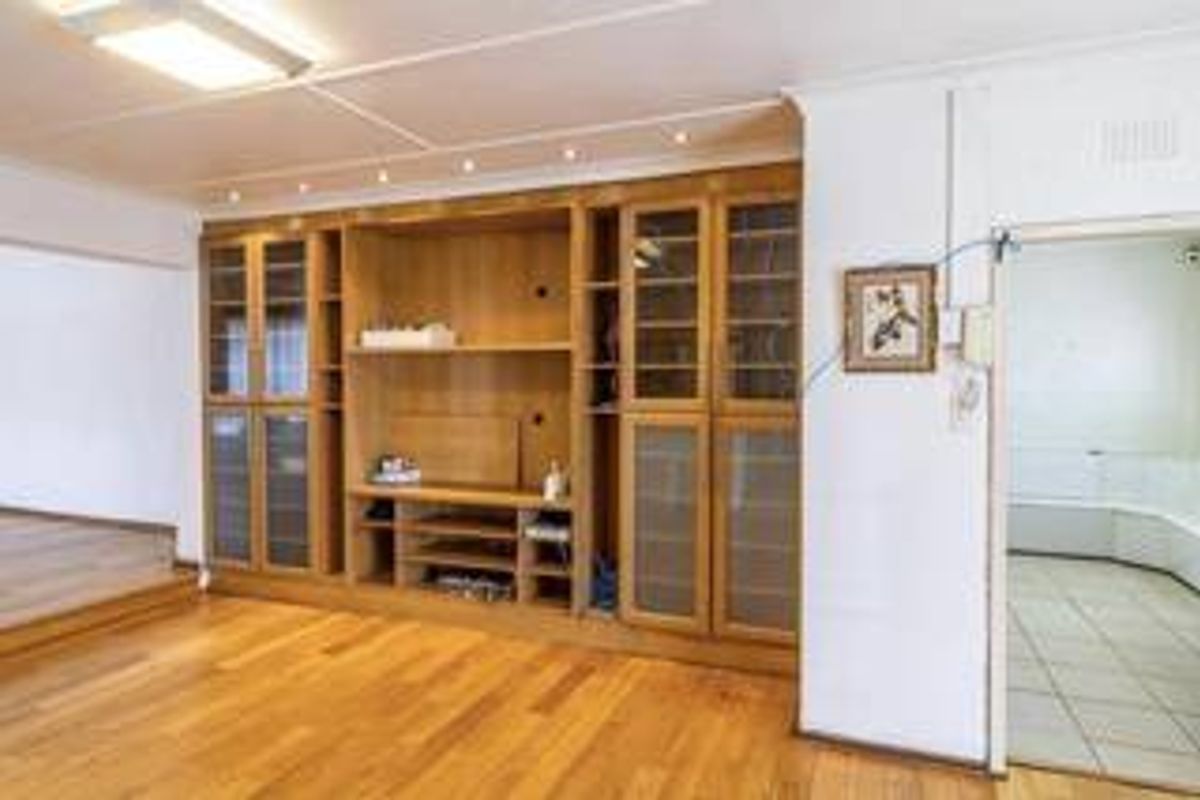 Spacious living area featuring extensive built-in wooden cabinetry, hardwood flooring, and recessed lighting, with an adjacent tiled room visible through the doorway.