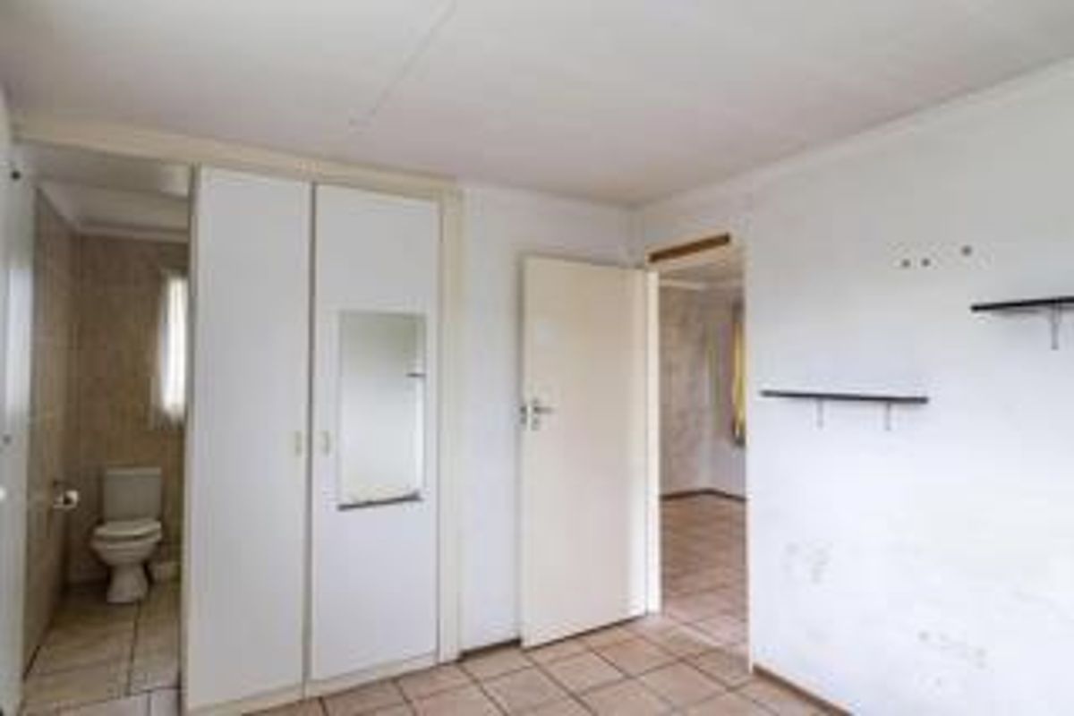 An empty bedroom featuring built-in cupboards, tiled flooring, and an attached en-suite bathroom with a toilet.
