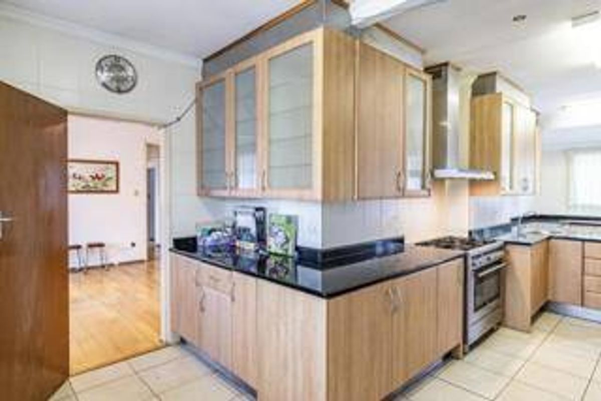 A functional kitchen featuring light wood cabinetry, dark granite countertops, stainless steel appliances, and tiled flooring, with an open flow to the adjacent living area.