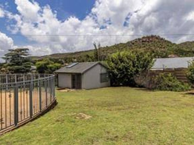 A spacious rear garden featuring a lawn, a swimming pool area with safety fencing, and a detached outbuilding with a solar water heater.