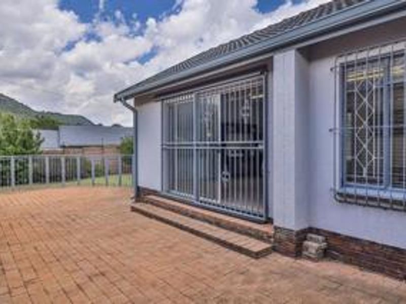 A paved outdoor patio area featuring a sliding glass door with security gates and bars, overlooking a garden with mountain views.