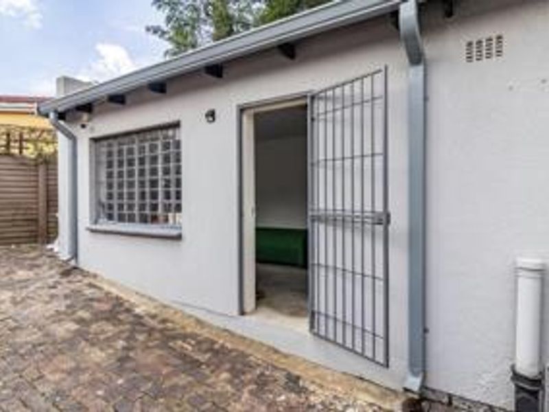 Rear exterior view of the property featuring brick paving, a security gate entrance, and a glass block window.