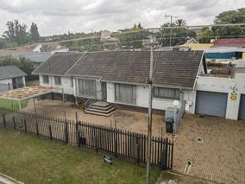 Elevated view of a single-story residential property featuring a tiled roof, double garage, carport, and paved driveway enclosed by metal perimeter fencing.