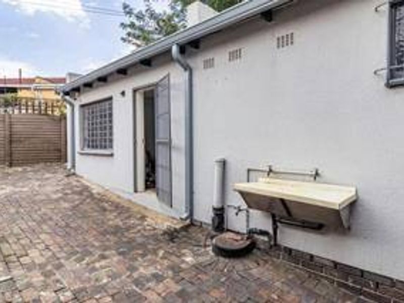 Rear exterior view of the property featuring brick paving, an external utility sink, and security bars on the windows.