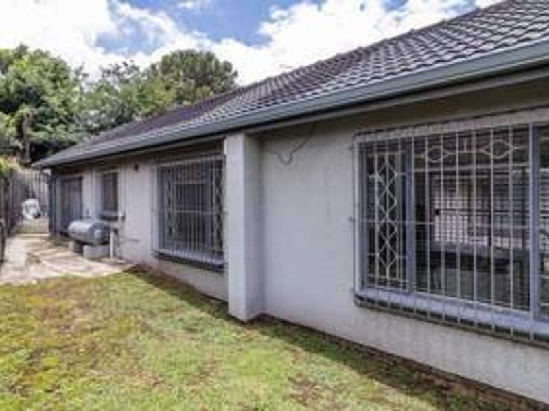 Rear exterior view of the house featuring a tiled roof, security bars on windows, and a small garden area.