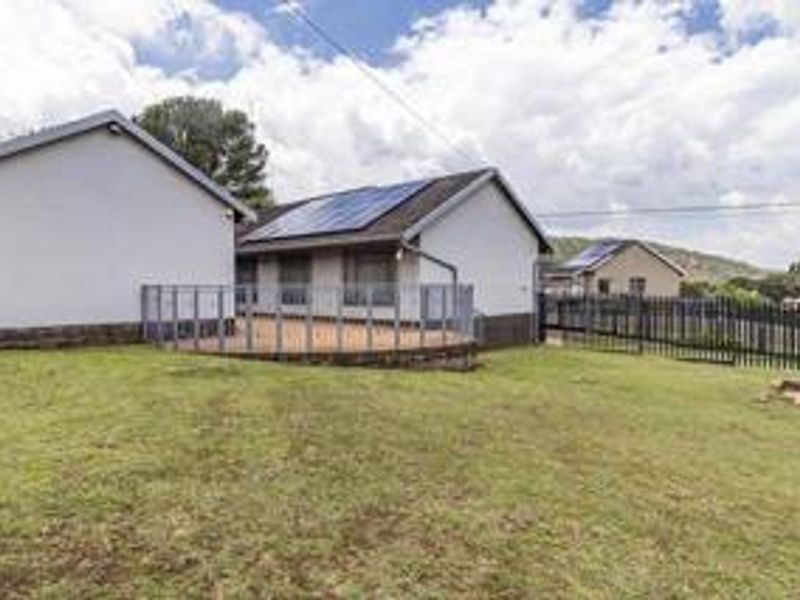 Rear view of the property featuring a raised patio area, solar panels on the roof, and secure metal perimeter fencing.