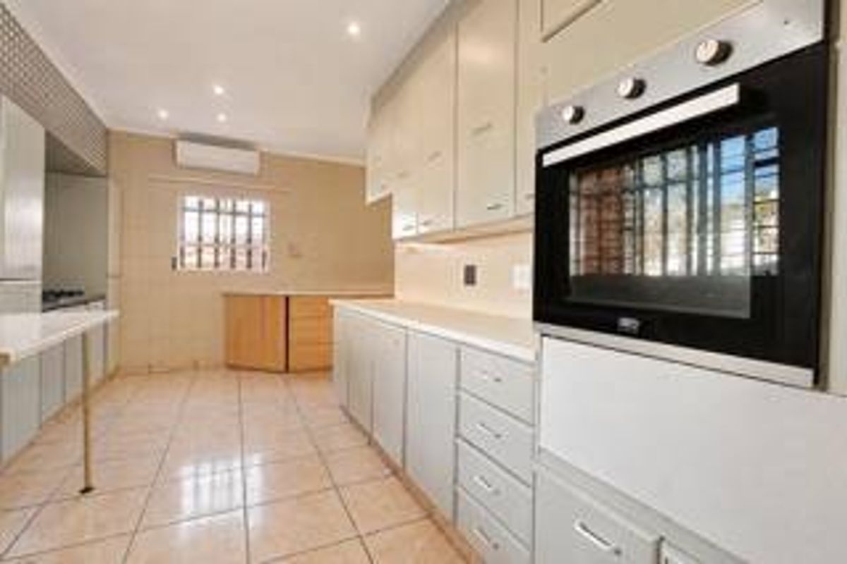 A functional kitchen featuring built-in cabinetry, a wall-mounted oven, tiled flooring, and a wall-mounted air conditioning unit.