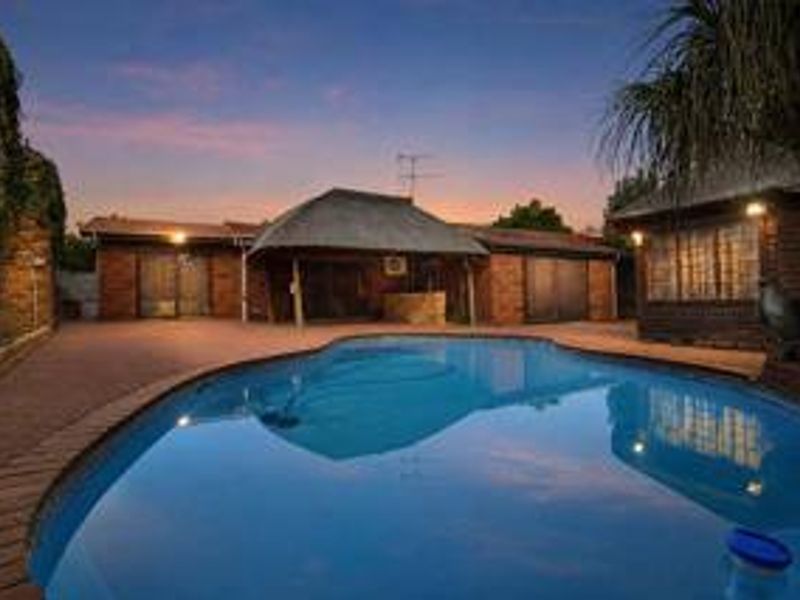 A well-maintained outdoor pool area featuring a swimming pool, brick exterior, and a covered patio space, perfect for evening relaxation.
