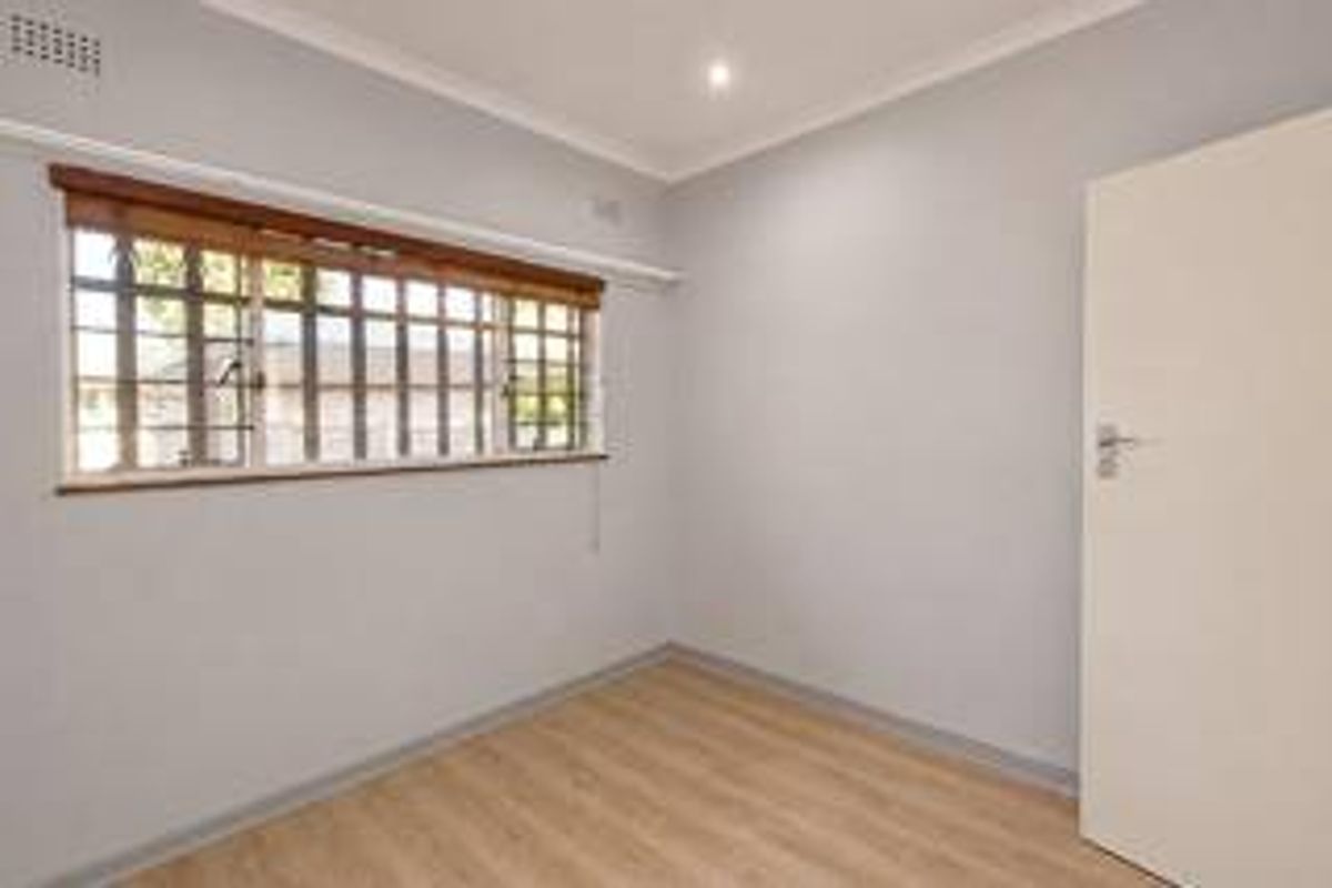 A clean, empty bedroom featuring light-toned laminate flooring, neutral walls, and a window fitted with security bars.