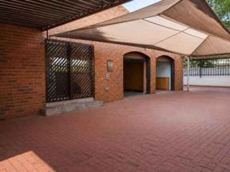 A paved driveway area featuring a double garage, shade sail covering, and exposed brick exterior walls.