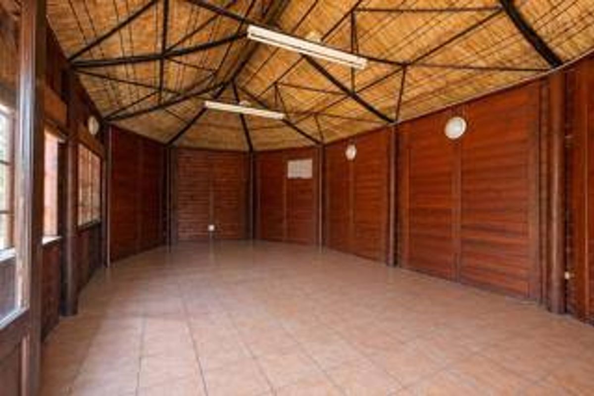Spacious living area featuring a unique thatched ceiling with exposed timber trusses, warm timber wall cladding, and durable tiled flooring.