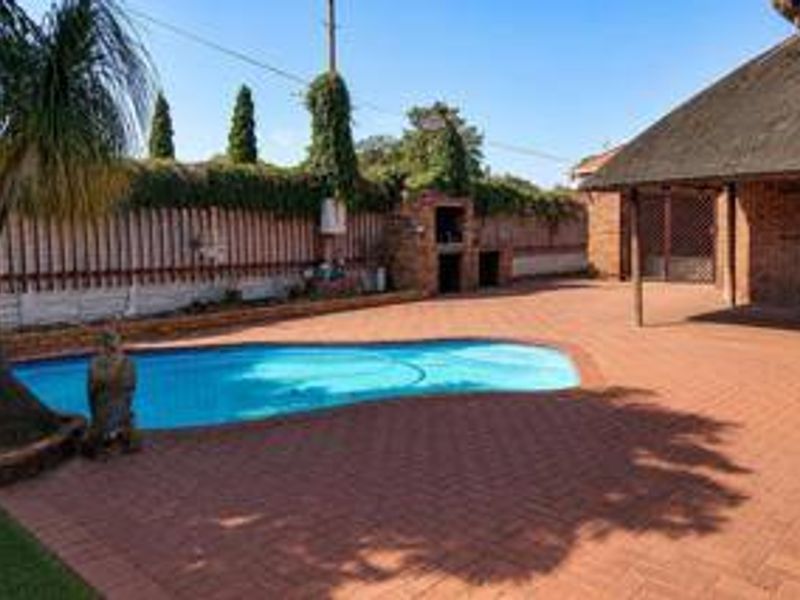 Outdoor entertainment area featuring a swimming pool, brick-paved patio, and a built-in braai, set against a private boundary wall.