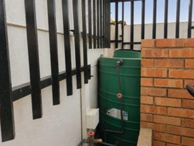 A utility area featuring a green water storage tank, brick walling, and metal security fencing.