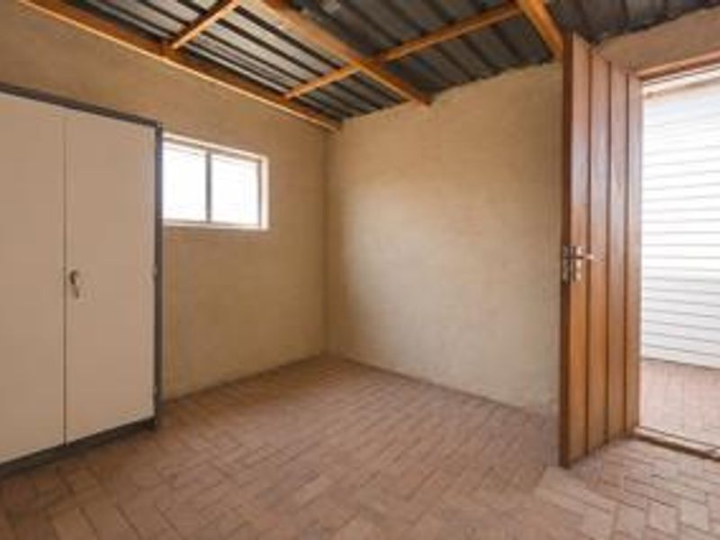 A functional utility space featuring brick flooring, exposed timber roof beams, and direct access to an outdoor area.