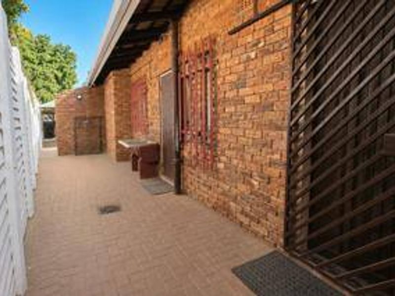 A side exterior walkway featuring exposed brick walls, security gates, and a small outdoor utility sink area.