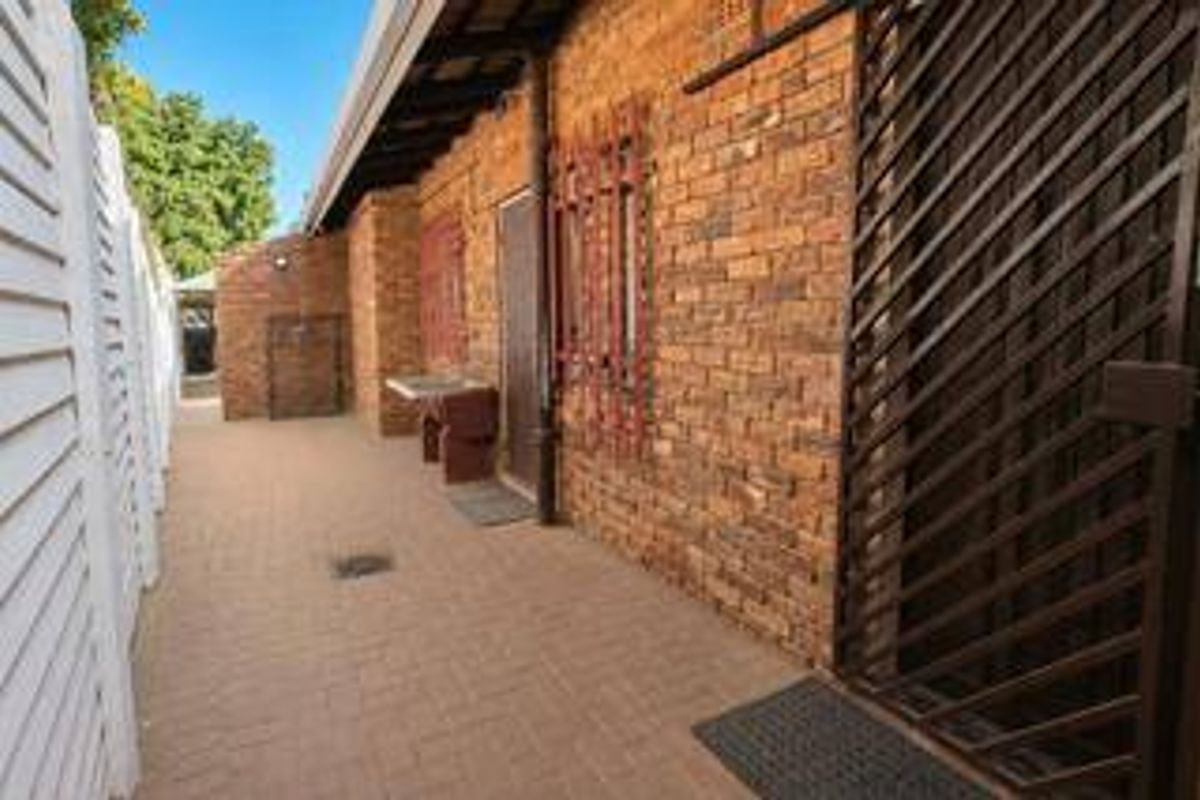 A side exterior walkway featuring exposed brick walls, security gates, and a small outdoor utility sink area.