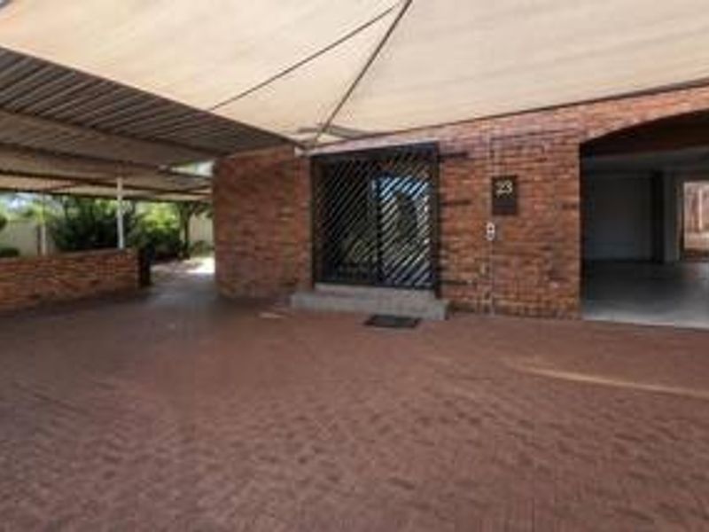Front exterior view featuring a brick facade, paved driveway, and a covered parking area with a shade sail.