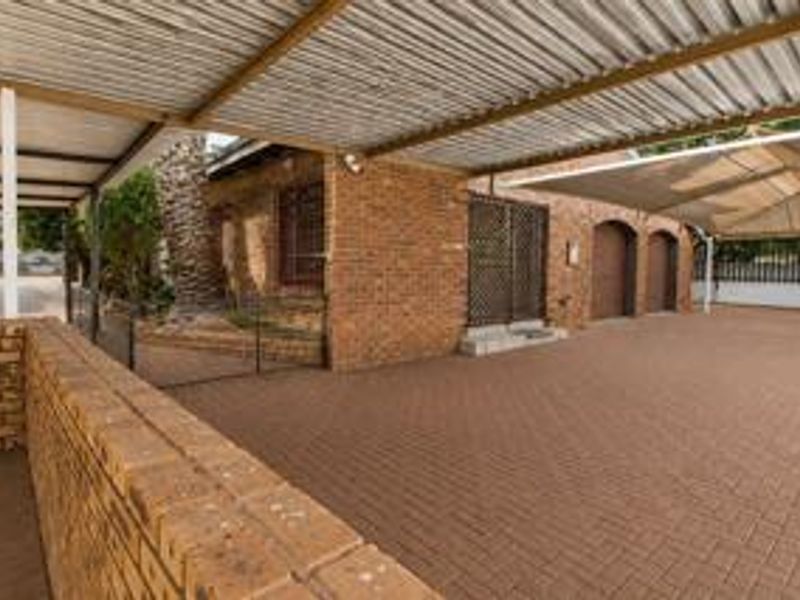 A spacious paved driveway area featuring a large corrugated metal carport, brick facade, and multiple garage access points.