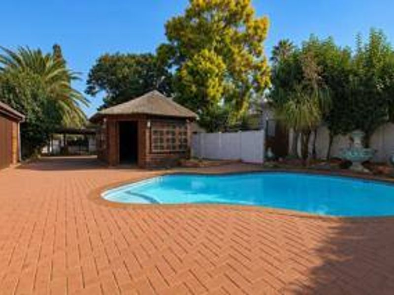 Outdoor pool area featuring a swimming pool, brick paved patio, and a thatched lapa structure, set within a landscaped garden.