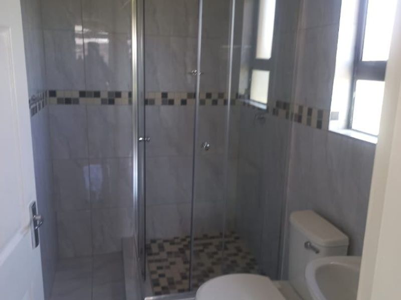 A functional bathroom featuring a glass shower enclosure, toilet, and pedestal basin with neutral wall and floor tiling.