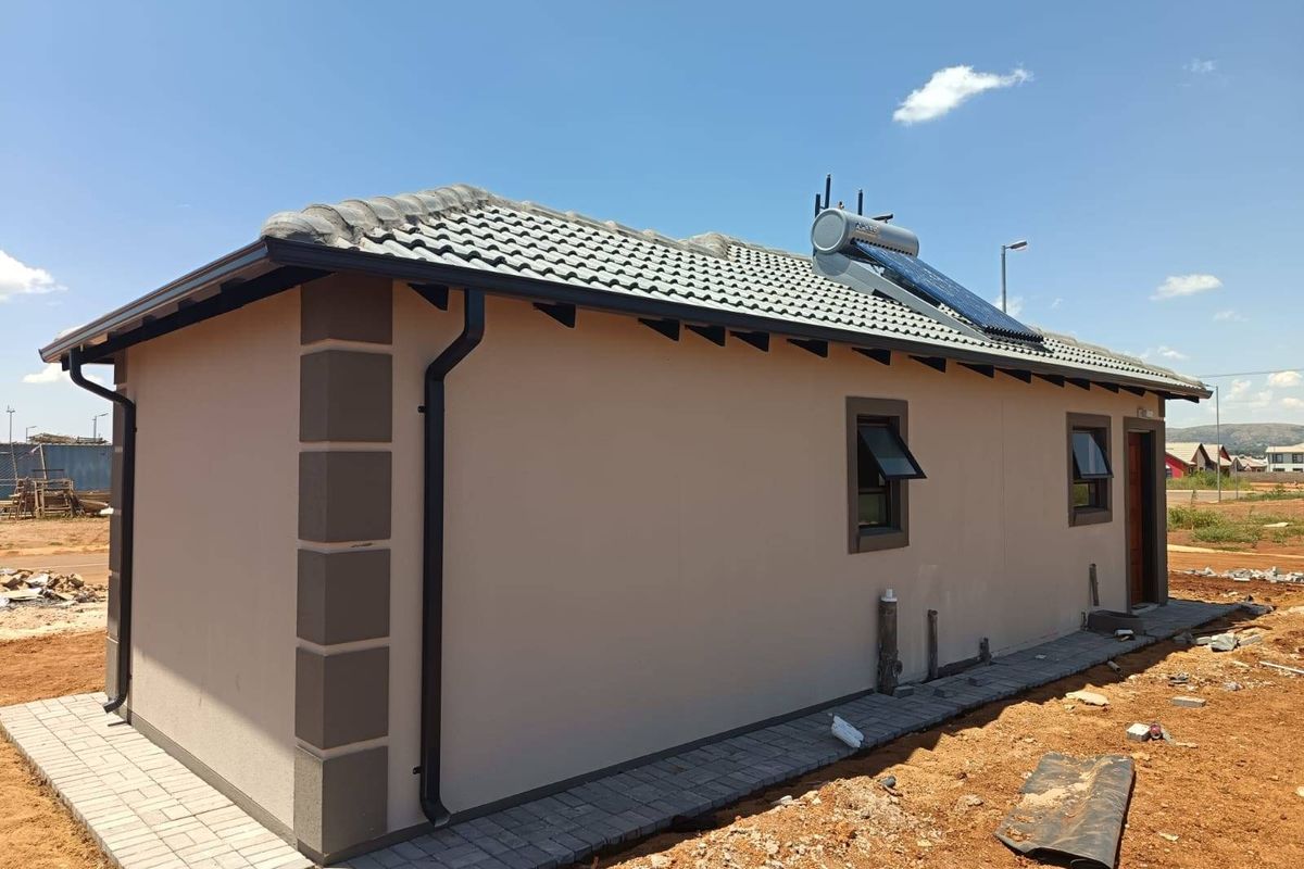 Rear view of a modern house featuring a tiled roof, solar water heating system, and paved perimeter walkway.