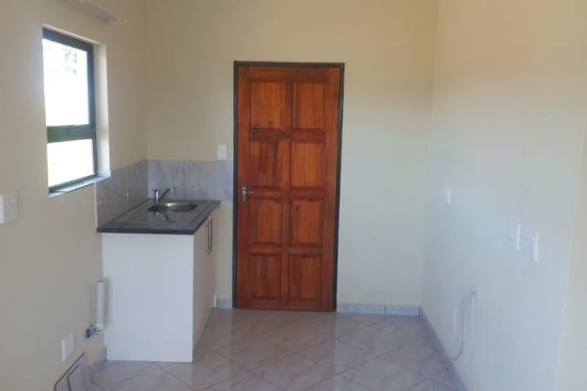 A compact, empty kitchen area featuring tiled flooring, a single sink unit with cabinetry, and a wooden door.