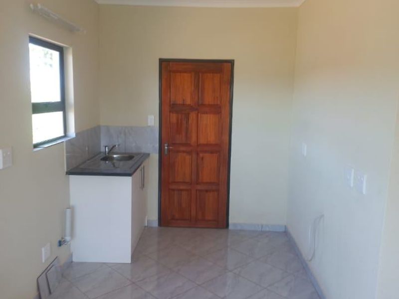 A compact, empty kitchen area featuring tiled flooring, a single sink unit with cabinetry, and a wooden door.