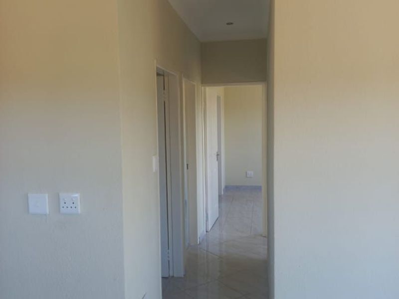 A clean, empty hallway featuring tiled flooring, recessed downlighting, and coved cornicing, providing access to multiple rooms within the property.