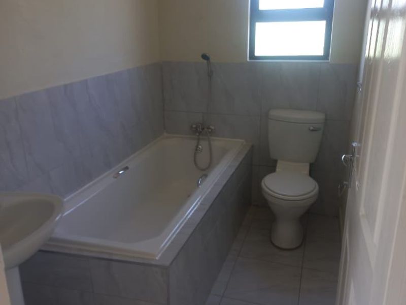 A functional bathroom featuring a bathtub, pedestal basin, and toilet with neutral tiled finishes and natural light from a window.