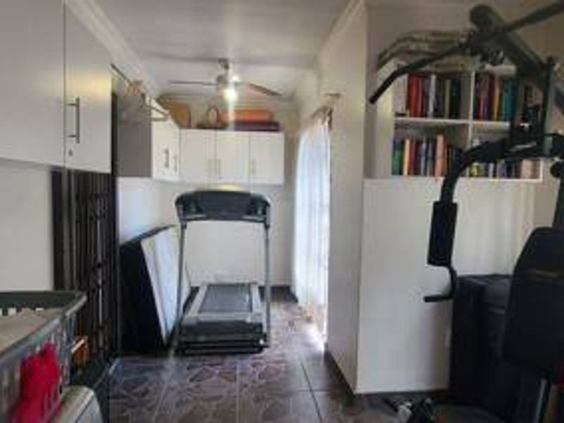 A functional home gym space featuring built-in cabinetry, overhead ceiling fan, and tiled flooring, currently utilized for fitness equipment and storage.
