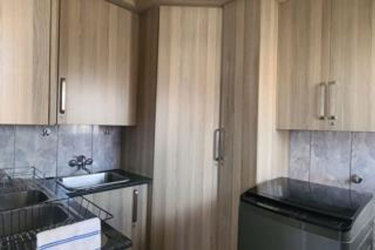 A functional kitchen area featuring light wood-tone cabinetry, stone countertops, a stainless steel sink, and tiled backsplash.