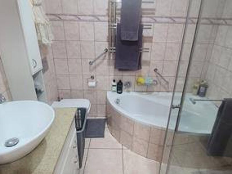 A functional bathroom featuring a vessel sink vanity, corner bathtub, glass-enclosed shower, and wall-mounted heated towel rail with neutral tiled finishes.