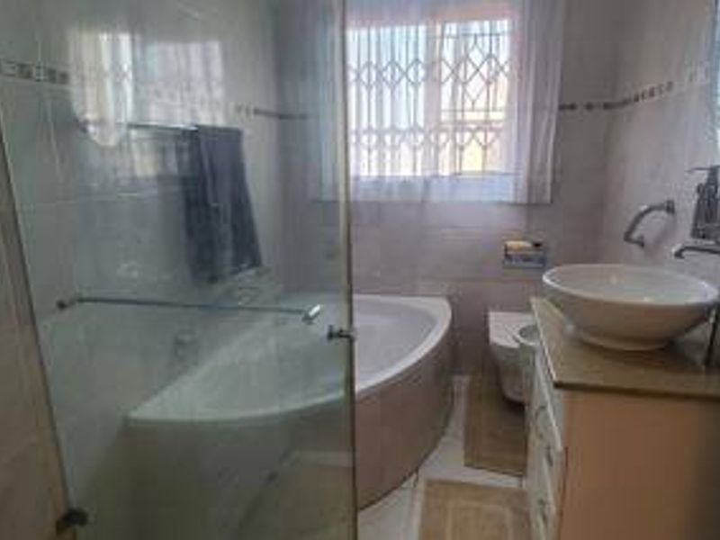 A functional bathroom featuring a corner bathtub, glass-enclosed shower, vessel sink vanity, and wall-mounted toilet with security bars on the window.