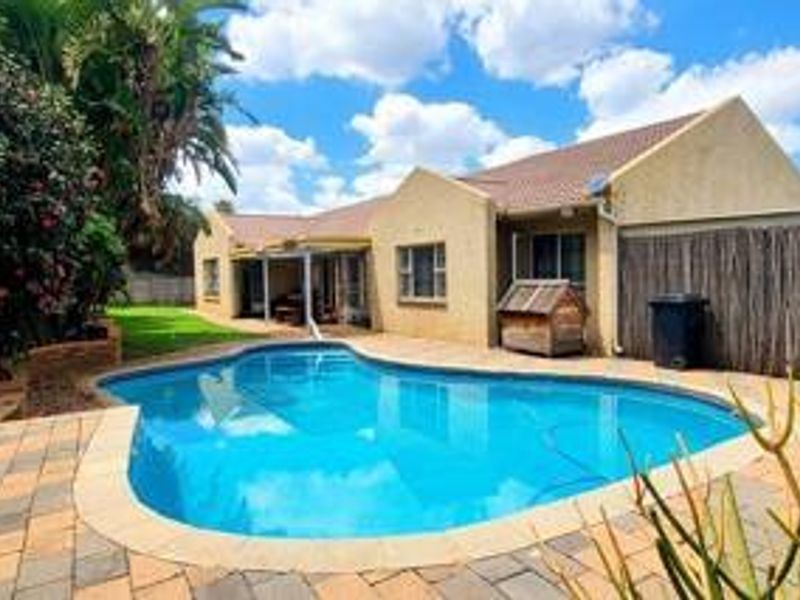 A well-maintained rear garden featuring a swimming pool, paved patio area, and covered outdoor space, ideal for relaxation and entertaining.
