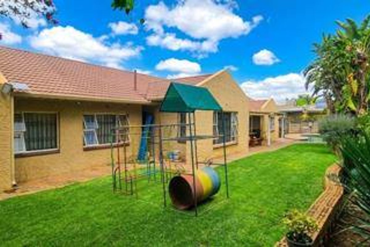 Rear view of the property featuring a tiled roof, security bars on windows, and a well-maintained lawn with a brick retaining wall.