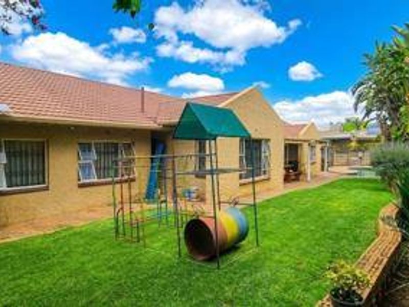 Rear view of the property featuring a tiled roof, security bars on windows, and a well-maintained lawn with a brick retaining wall.