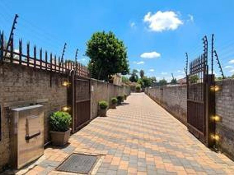A secure entrance driveway featuring paved surfaces, high brick boundary walls with electric fencing, and integrated security gate lighting.
