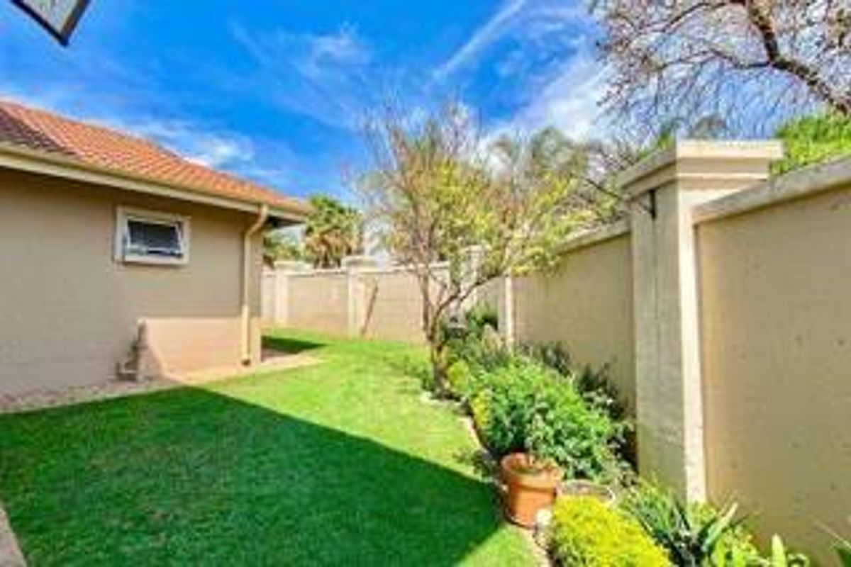 A well-maintained rear garden area featuring a manicured lawn, perimeter boundary walls, and a view of the house exterior with a tiled roof.