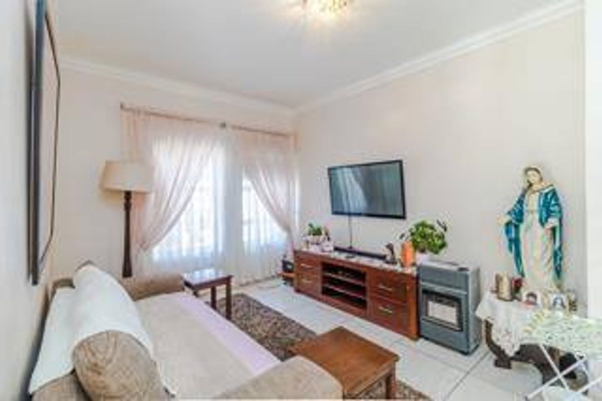 A comfortable living room featuring tiled flooring, ceiling cornicing, and a sliding glass door providing natural light.